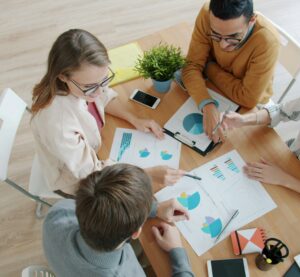 Vier Personen sitzen an einem Tisch. Auf diesem liegen Blätter mit verschiedenen Diagrammen. Sie Zeigen sich Sachen und disktuieren.
