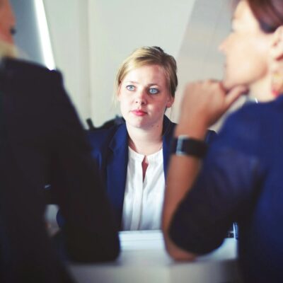 Bei einem Personalgespräch sitzt eine Mitarbeiterin im Mittelpunkt, während zwei weitere Personen aufmerksam zuhören und sich an dem Gespräch beteiligen.