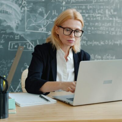 Eine Frau mit Brille sitzt an einem Laptop. Daneben liegen Stift und Notizblock.