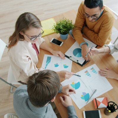 Vier Personen sitzen an einem Tisch. Auf diesem liegen Blätter mit verschiedenen Diagrammen. Sie Zeigen sich Sachen und disktuieren.