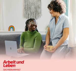Eine Frau sitzt mit Laptop auf dem Schoß auf einer Couch. Eine zweite sitzt auf der Lehne und neigt zu ihr hinunter, sie hat eine Tasse in der Hand.
