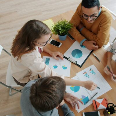 Vier Personen sitzen an einem Tisch und sprechen über die Grafiken, die auf dem Tisch liegen. Wir schauen von oben auf die Gruppe.